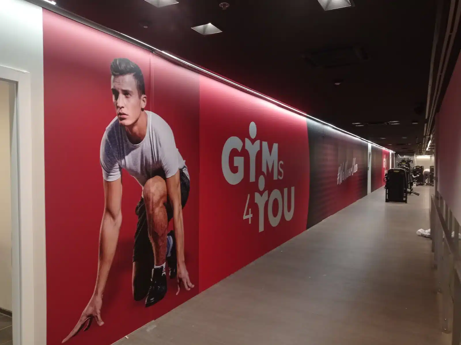 Zidna foto tapeta s motivom sportaša i logotipom duž hodnika teretane